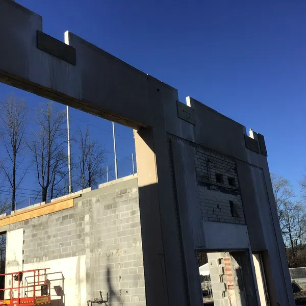 Concrete and brick building under construction with blue sky and leafless trees in the background.