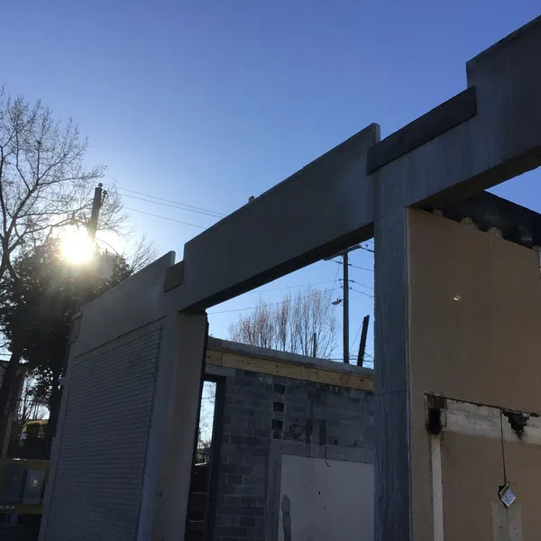 Partially constructed concrete building with clear blue sky and sun shining through trees in the background
