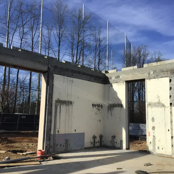 Partially constructed building with concrete walls and large window and door openings under a clear blue sky.