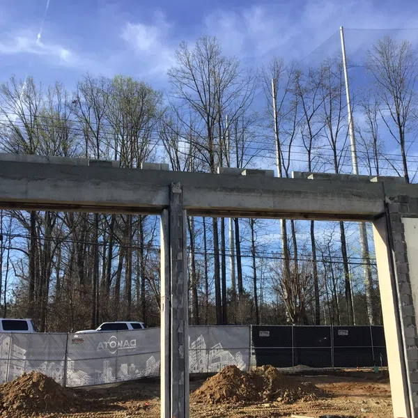 Construction site with concrete walls and framework against a backdrop of leafless trees and blue sky.