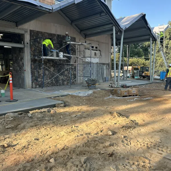 Construction workers repair and renovate building exterior with scaffolding and stone facade under a metal roof.
