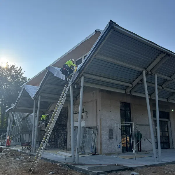Construction workers installing metal roofing on a modern building under clear blue sky during daytime.