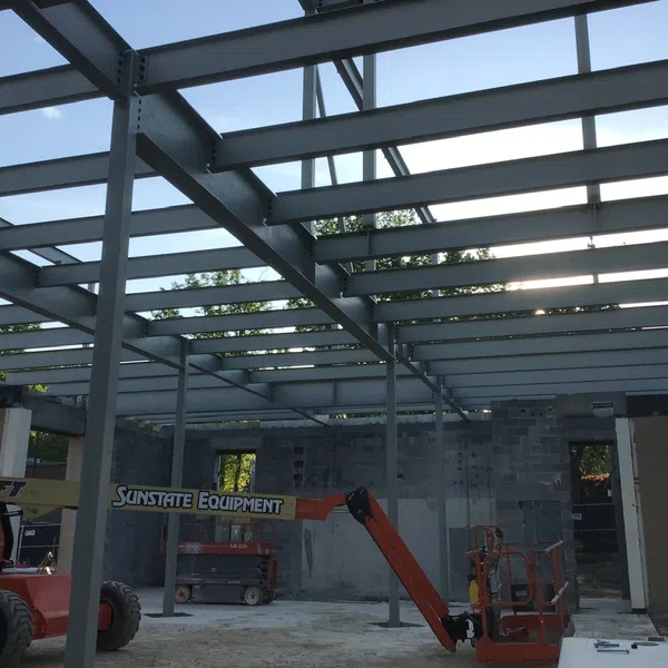Steel framework and construction equipment inside a partially built industrial building with concrete block walls.