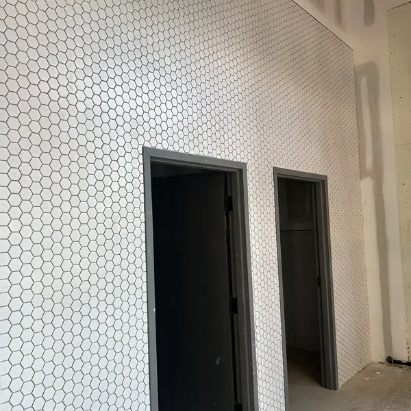 Interior wall covered with white hexagonal tiles featuring two dark gray doorways in a construction area.