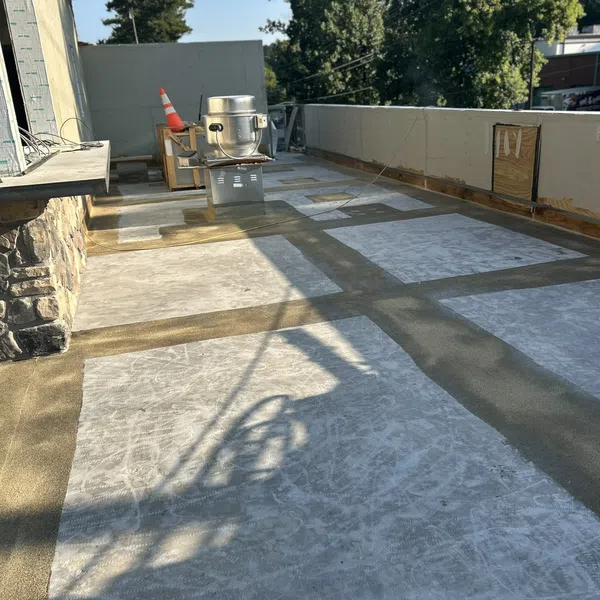Outdoor rooftop under construction with concrete slabs, ventilation equipment, and safety cone in daylight