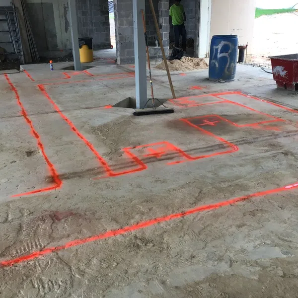 Indoor construction site with neon orange layout markings on the concrete floor and tools scattered around.