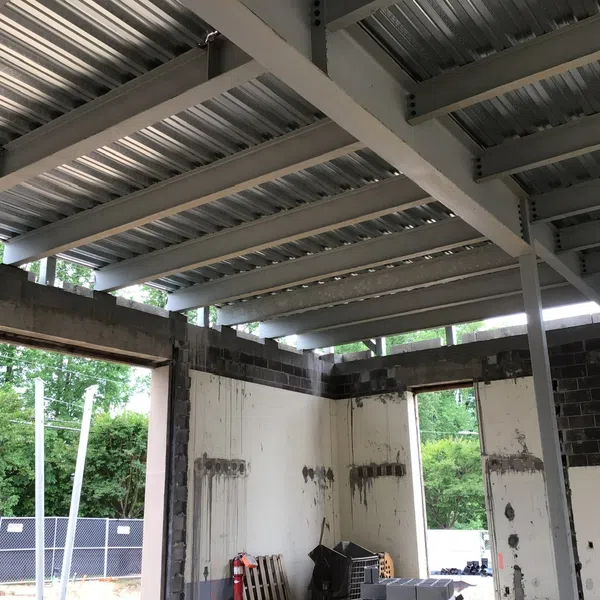 Interior of an unfinished building with steel beams, concrete block walls, and an open window showing greenery outside.