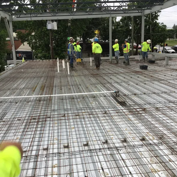 Construction workers installing steel rebar grid for concrete floor slab on a building site under an open frame structure.