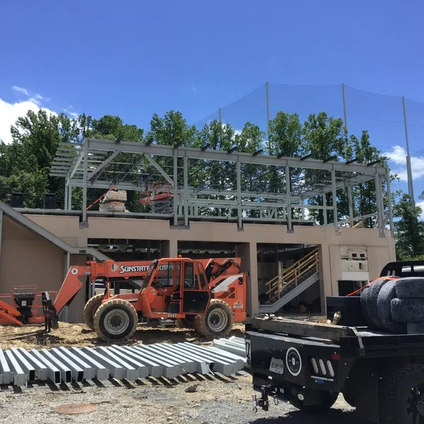 Construction site with steel framework, orange heavy machinery, and building materials under a blue sky.