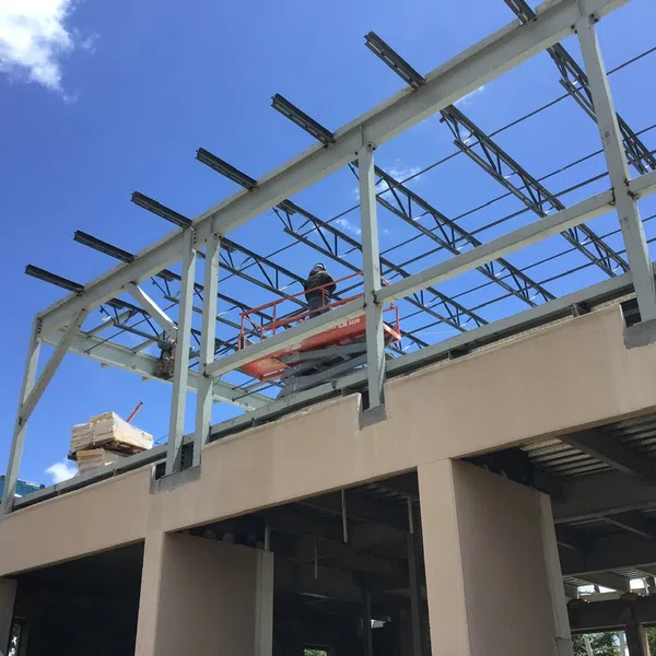 Construction worker on lift working on steel frame of building under clear blue sky.