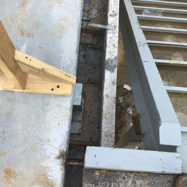 Close-up of concrete foundation with wooden support beam and steel framing on construction site.