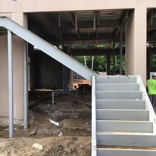 Steel staircase structure under construction with workers in safety gear on a building site with exposed earth and framework.