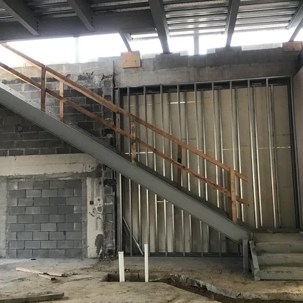Industrial interior with metal staircase, concrete block wall, steel framing, and exposed ceiling beams under construction.