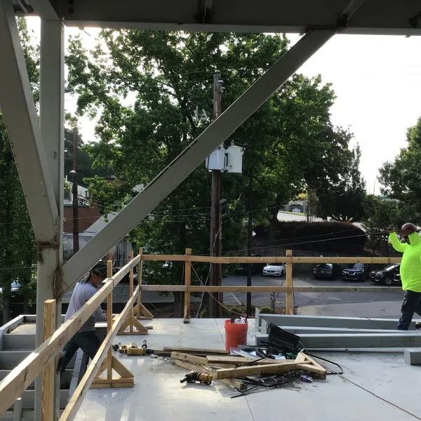 Construction workers on a building site with safety railing and steel beams during daytime work.