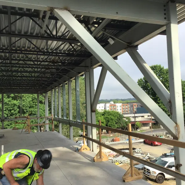 Construction worker wearing safety vest and helmet working on a steel-framed building under construction.