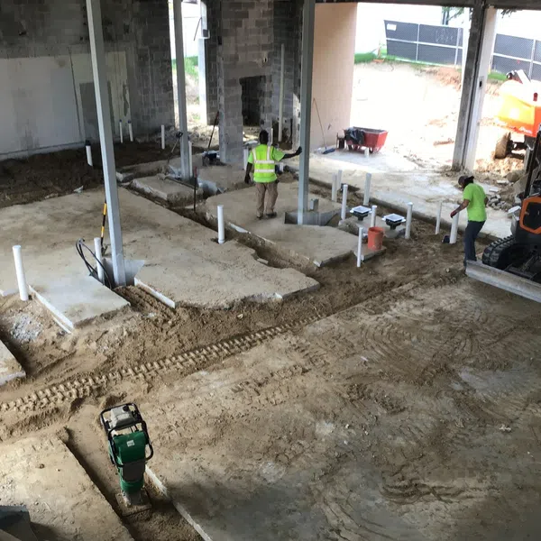 Construction site with workers, exposed foundation, pipes, and machinery inside a partially built structure