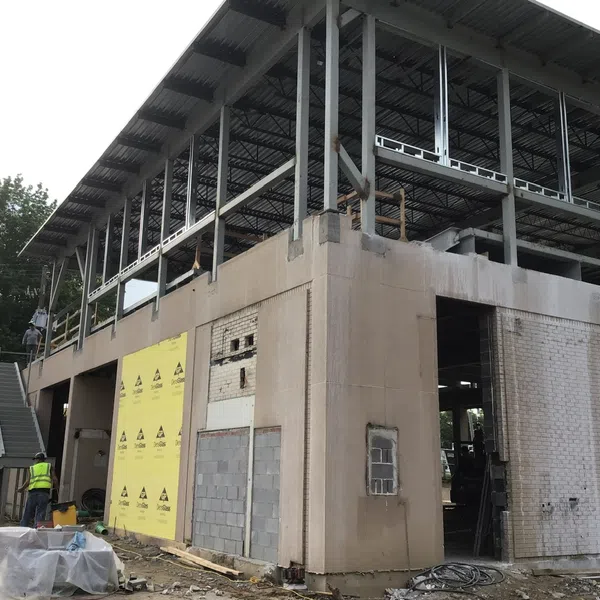 Two-story building under construction with steel framework and concrete walls surrounded by construction materials and workers.