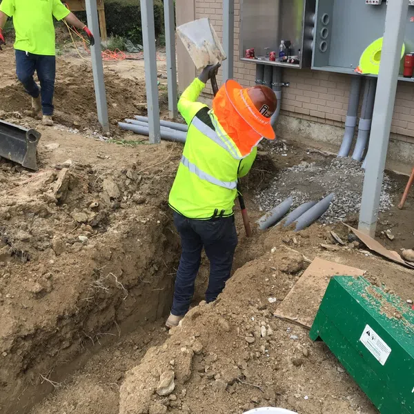 Construction workers in safety gear working on underground piping at a residential building site.
