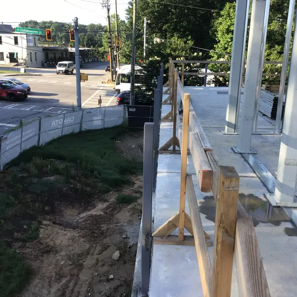 Construction site with steel frame and wooden safety rails next to a busy urban intersection with cars and traffic lights.