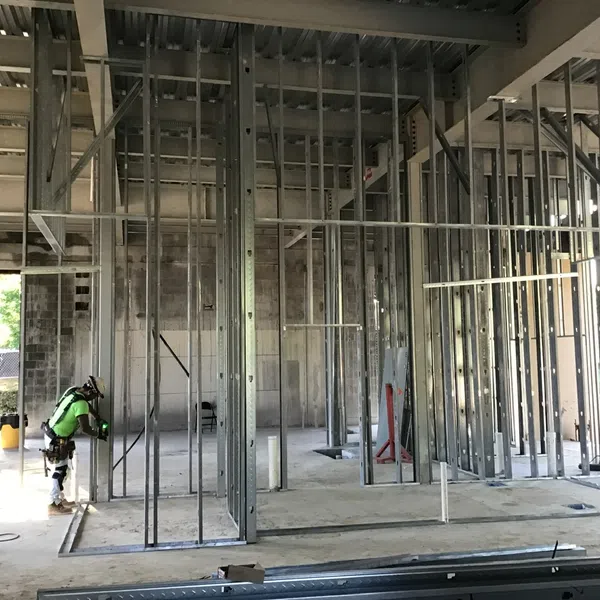 Construction worker in safety gear assembling metal framing inside a partially built commercial building.