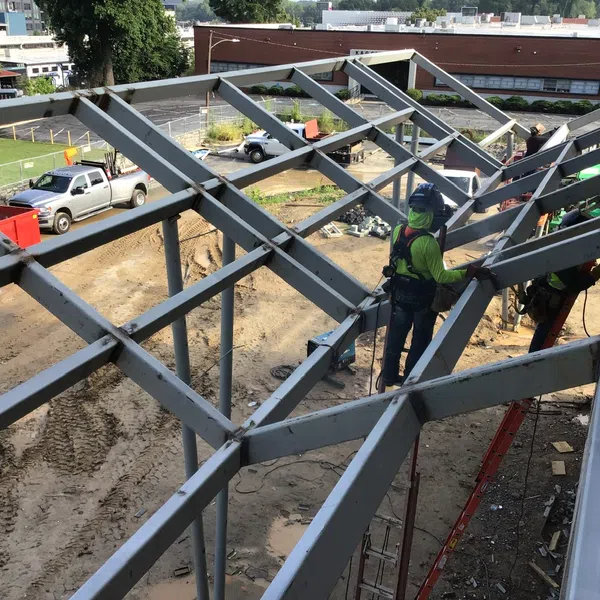 Construction workers assemble steel framework on an outdoor building site with trucks and equipment nearby.