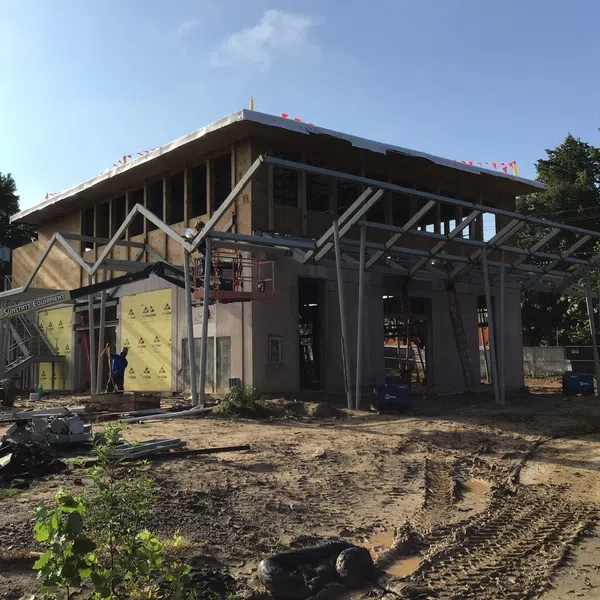 Two-story building under construction with steel framing and workers installing exterior panels on a sunny day.