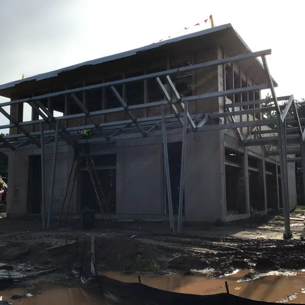 Two-story house under construction with steel framework and muddy construction site in daylight.