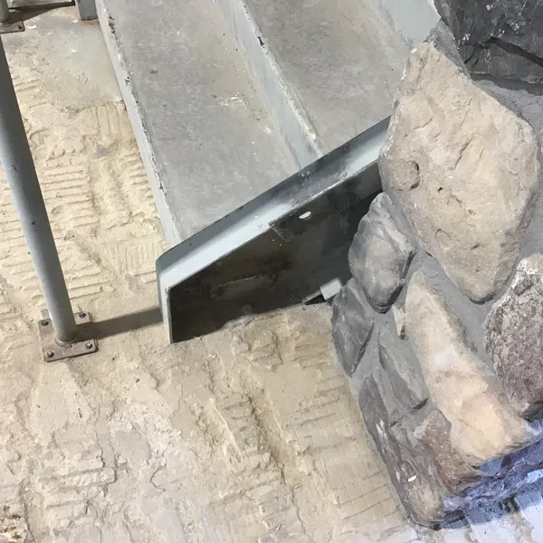 Modern stone pillar with cobblestone texture next to metal stair rail on concrete floor with visible tire marks.