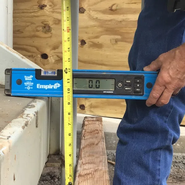 Person measuring vertical alignment with digital level and tape measure on construction site.