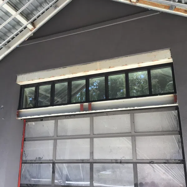 Gray building wall with black-framed windows and a commercial garage door under a metal roof.