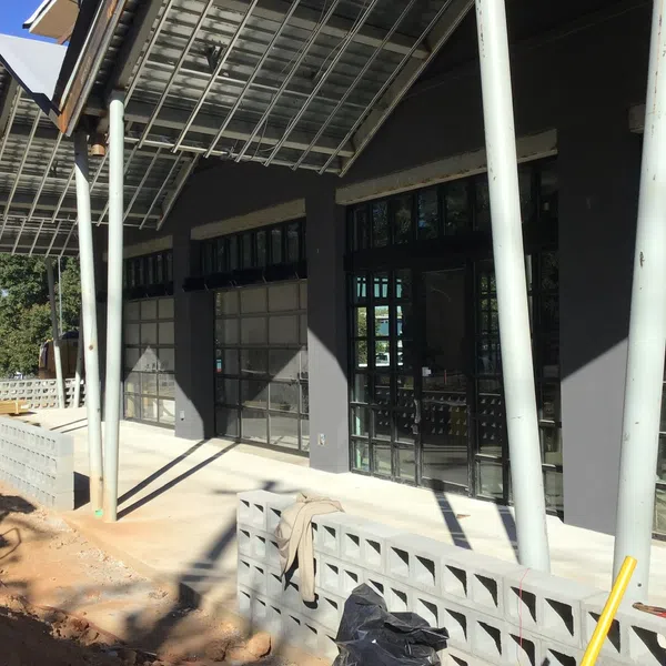 Modern building facade with large glass windows, angled metal roof, and a concrete block wall in sunlight.