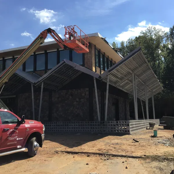 Construction site with a modern building, a red truck with lift, and workers under a partially covered patio.