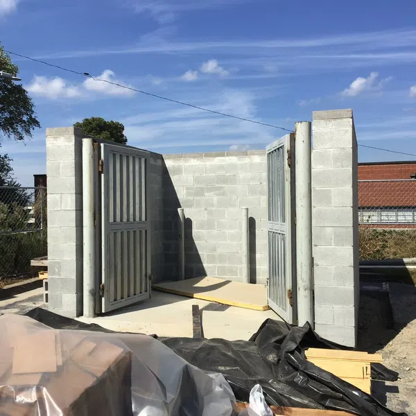Partially constructed concrete block structure with metal doors open on a sunny day at a construction site.