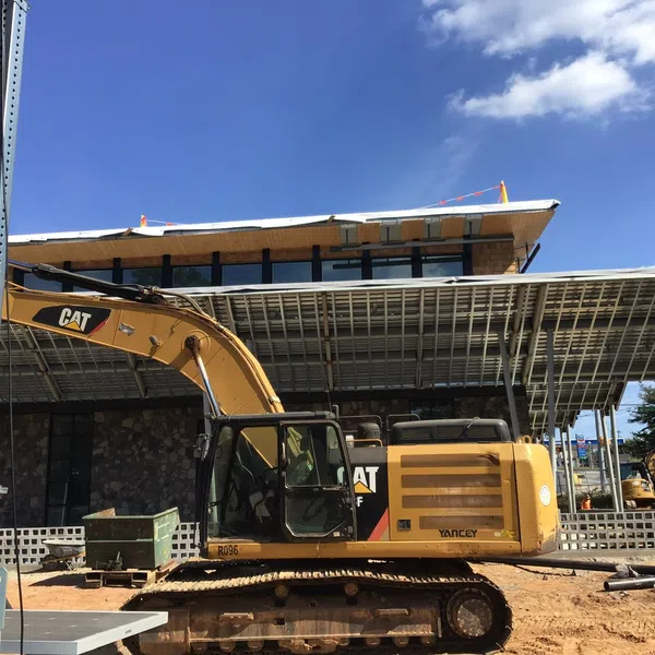 Yellow CAT excavator parked at construction site with modern building and blue sky in background