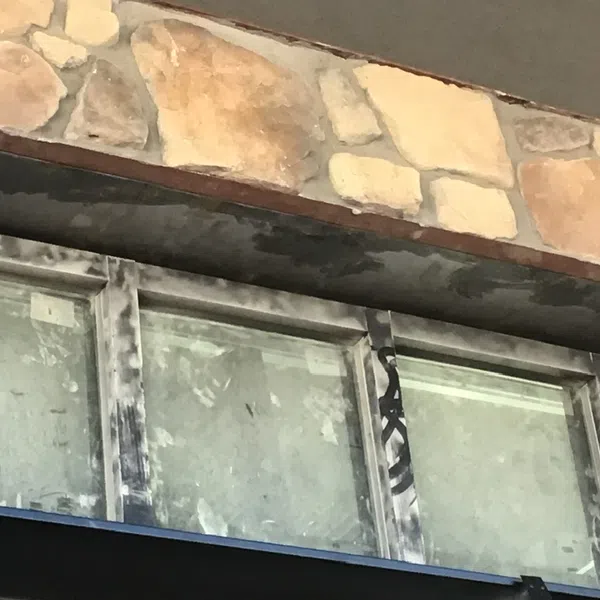 Close-up of weathered metal window frames beneath a stone wall with varied beige and tan rocks.