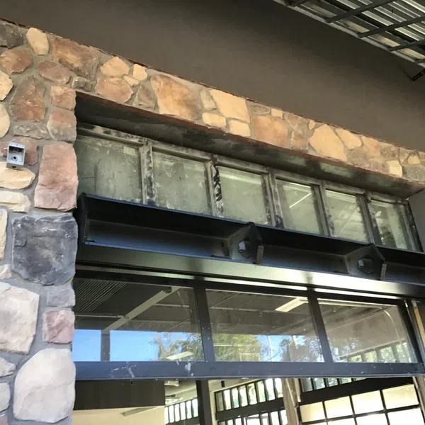 Stone wall facade with rectangular windows and black metal awning under a metal roof overhang.