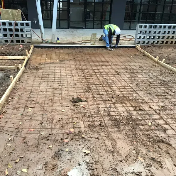 Construction worker installing wire mesh for concrete driveway at building entrance under construction.