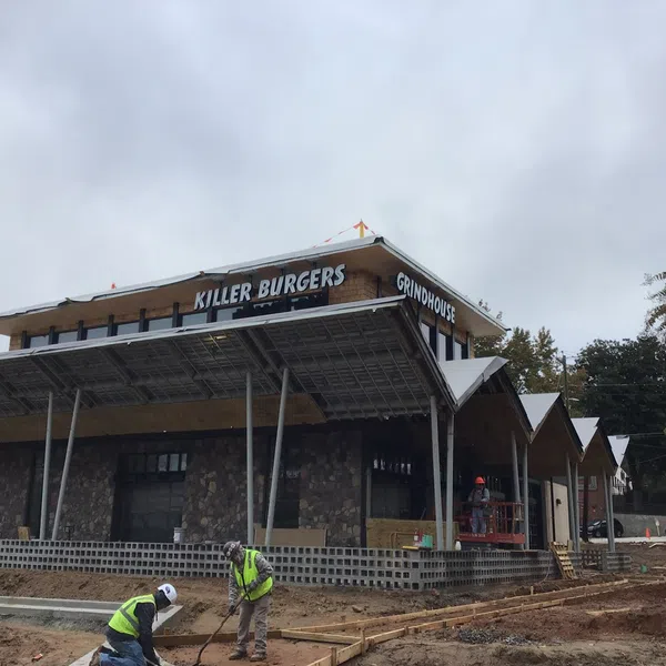 Workers in safety vests build the exterior of the Killer Burgers Grindhouse restaurant under a cloudy sky.