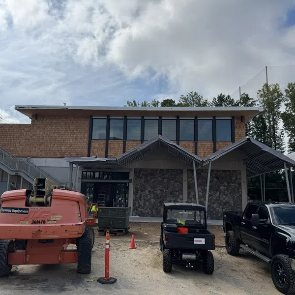 Under-construction modern building with stone wall and vehicles parked outside under partly cloudy sky