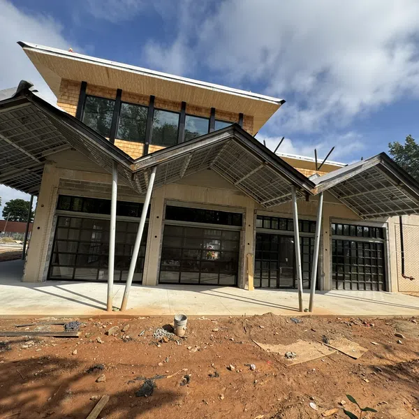 Modern building under construction with large glass doors and angled metal canopies on a sunny day.