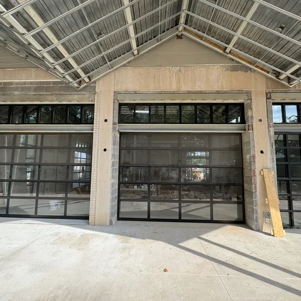 Modern black metal framed glass garage doors in an unfinished concrete building under a metal roof.
