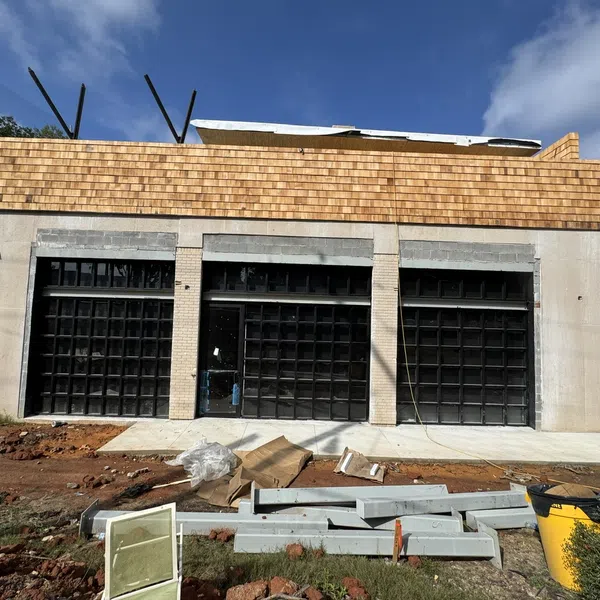 Modern building under construction with large black grid windows and wooden paneling on top under blue sky