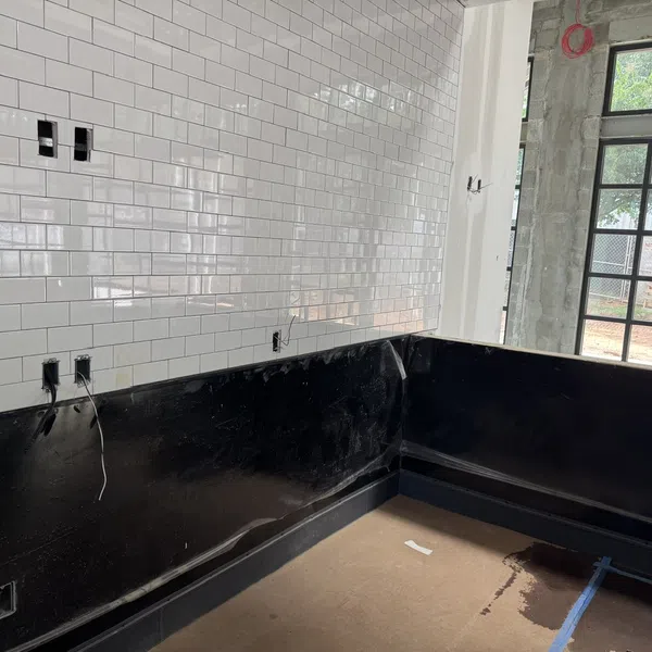 Interior corner with white subway tiles and black paneling under construction near large window.