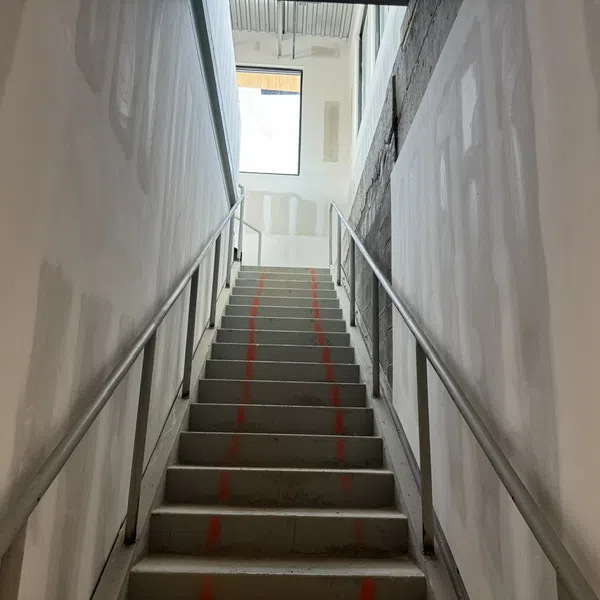 Industrial concrete staircase with metal railings and red guidelines in an unfinished building interior.