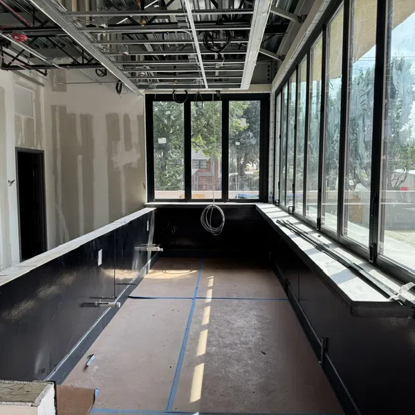 Interior of a room under construction with large windows, exposed ceiling, and black lower walls.