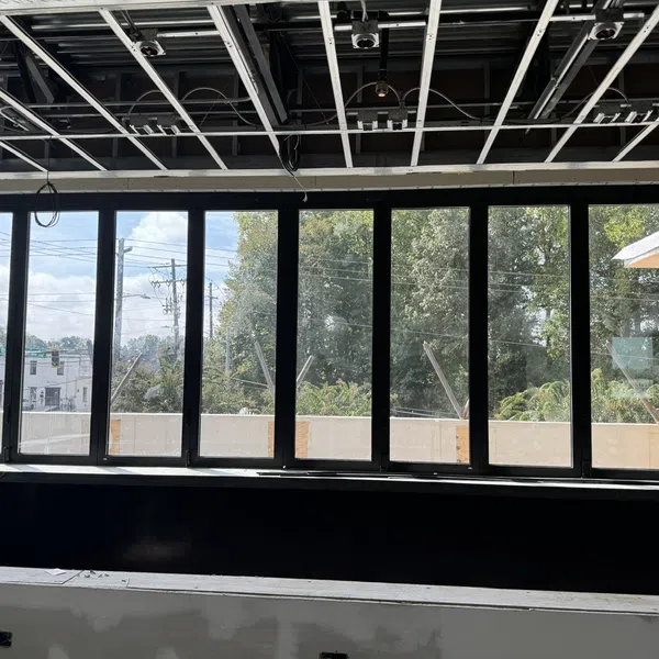 Large black-framed windows in a partly constructed room with exposed ceiling and outdoor greenery visible.