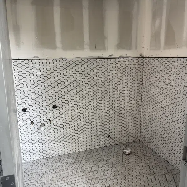 Bathroom under construction with white hexagonal tile flooring and wall tiling partially installed