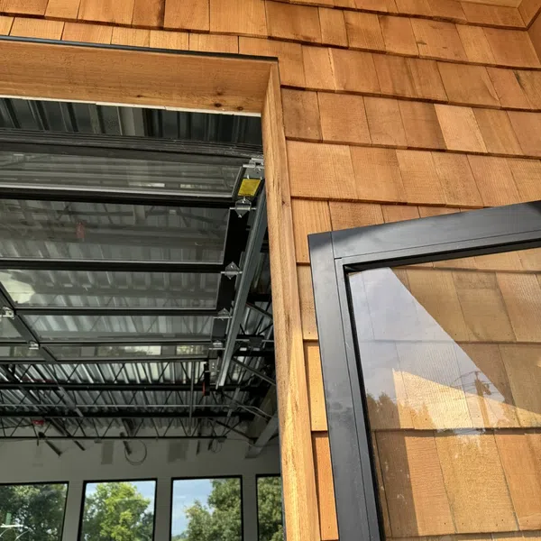 Close-up of wooden shingle siding and window frame with industrial interior and multiple windows visible inside.