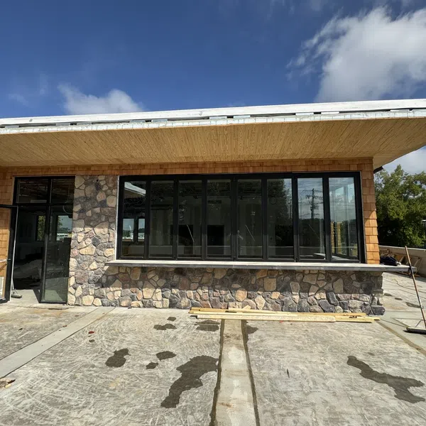 Modern building exterior with stone and wood siding under a blue sky with scattered clouds.