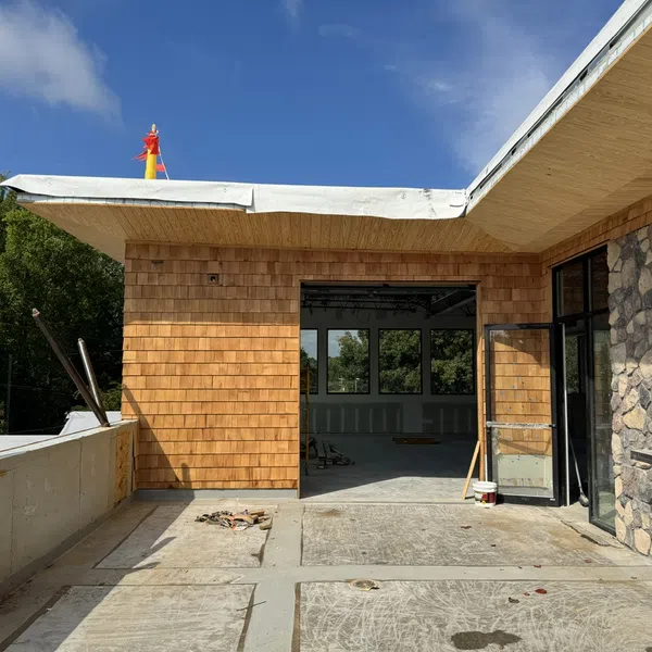 Partially constructed modern building with stone and wood siding under a clear blue sky.